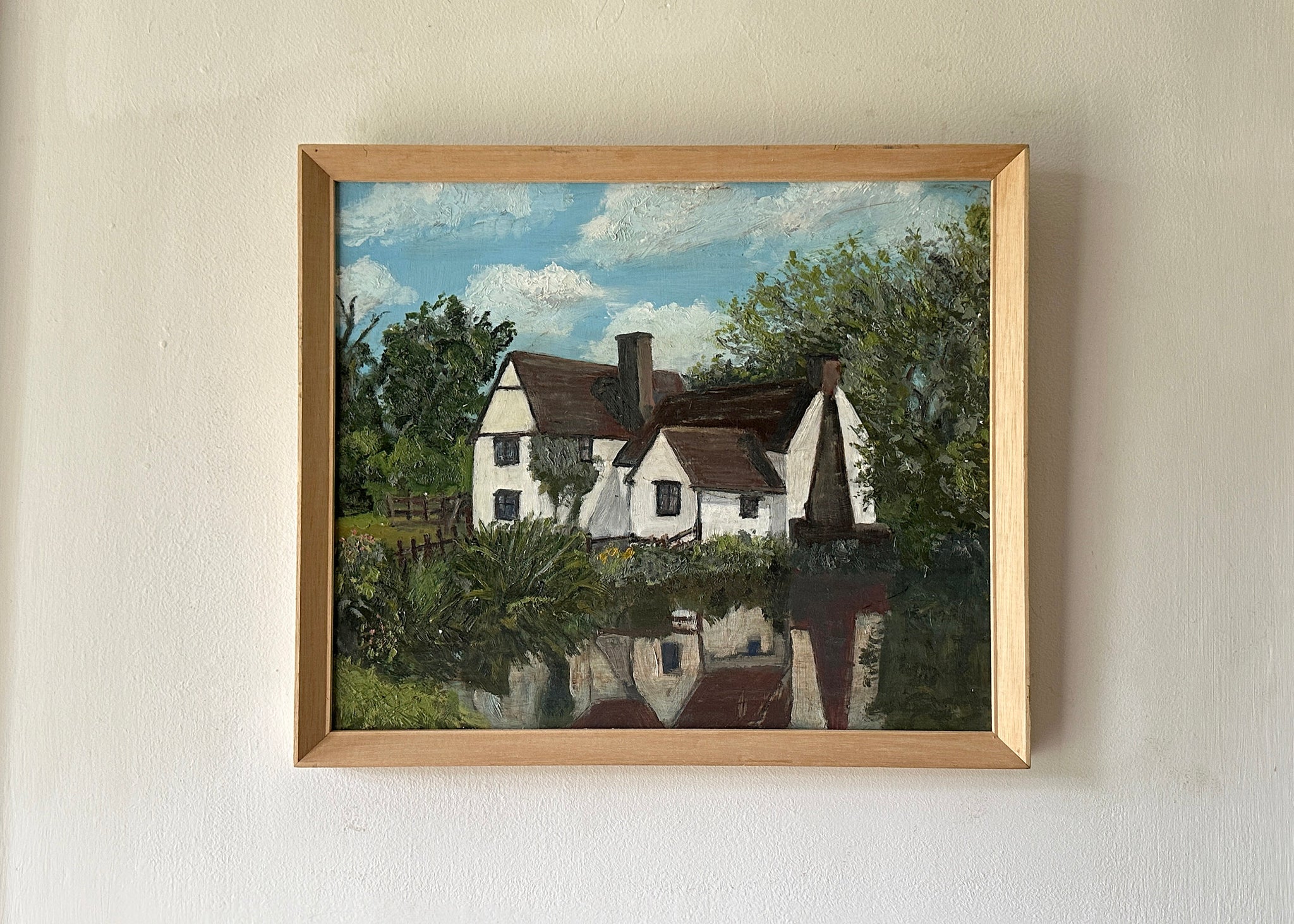 Framed painting of a house with a landscape background on a beige wall